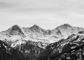 Black and white photo capturing majestic, snow-capped mountains in a serene winter landscape.
